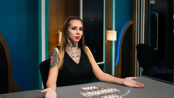 Profesionální krupiérka během živé hry v kasinovém prostředí Krupiérka s tetováním sedí u stolu v kasinovém studiu a prezentuje karty na stole